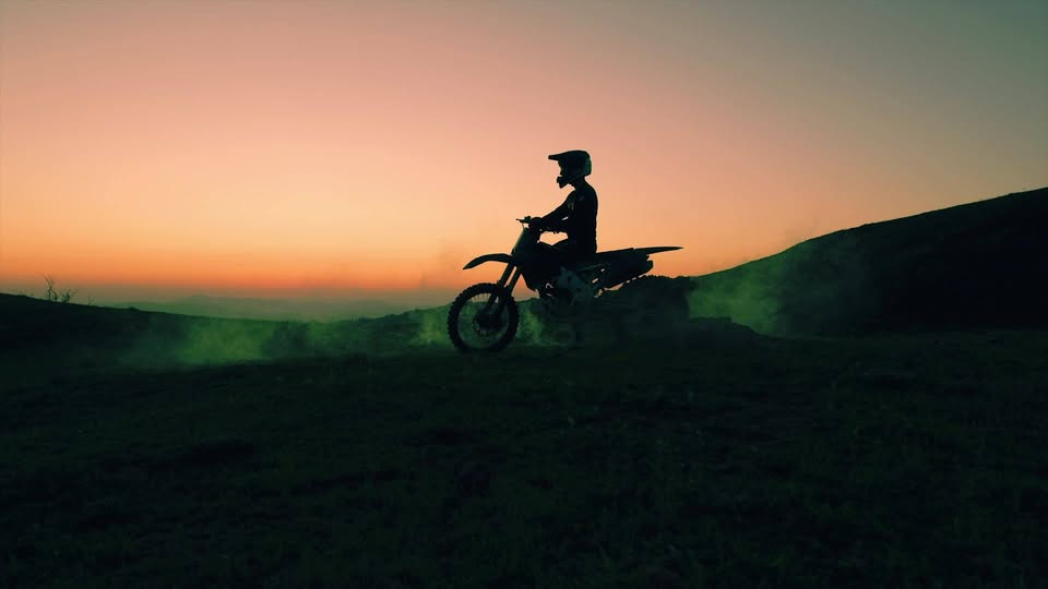 Motociclista en una moto de enduro sobre un cerro al atardecer